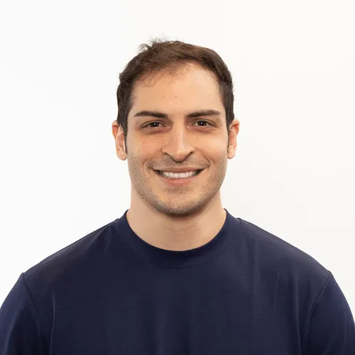 Smiling man with short dark hair wearing a dark blue crew-neck shirt against a plain white background.