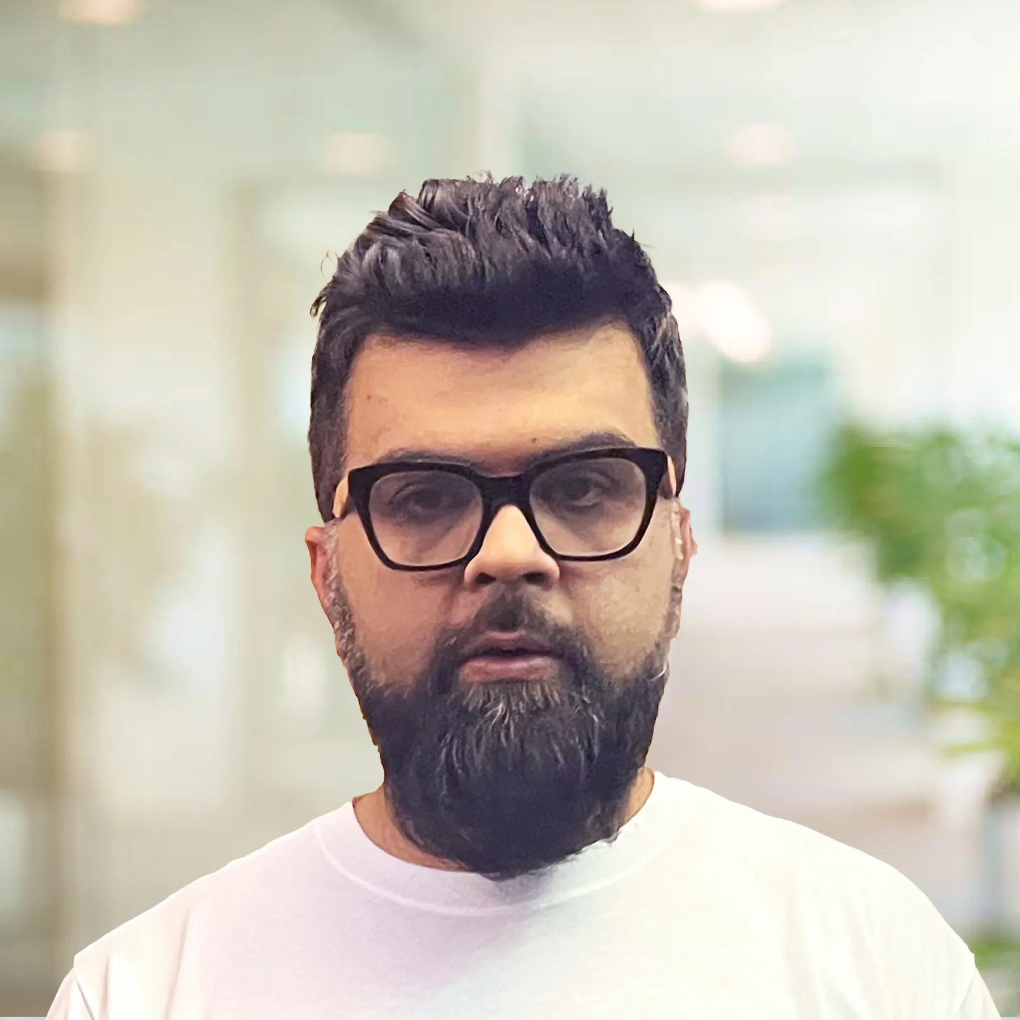 Young man with dark hair and beard wearing a white shirt looking to the side in a softly lit indoor setting.