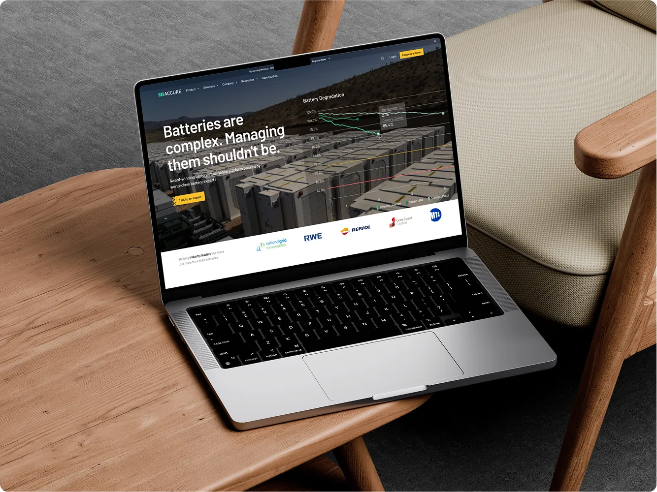 Open laptop on a wooden table displaying a battery management platform with charts and client logos.