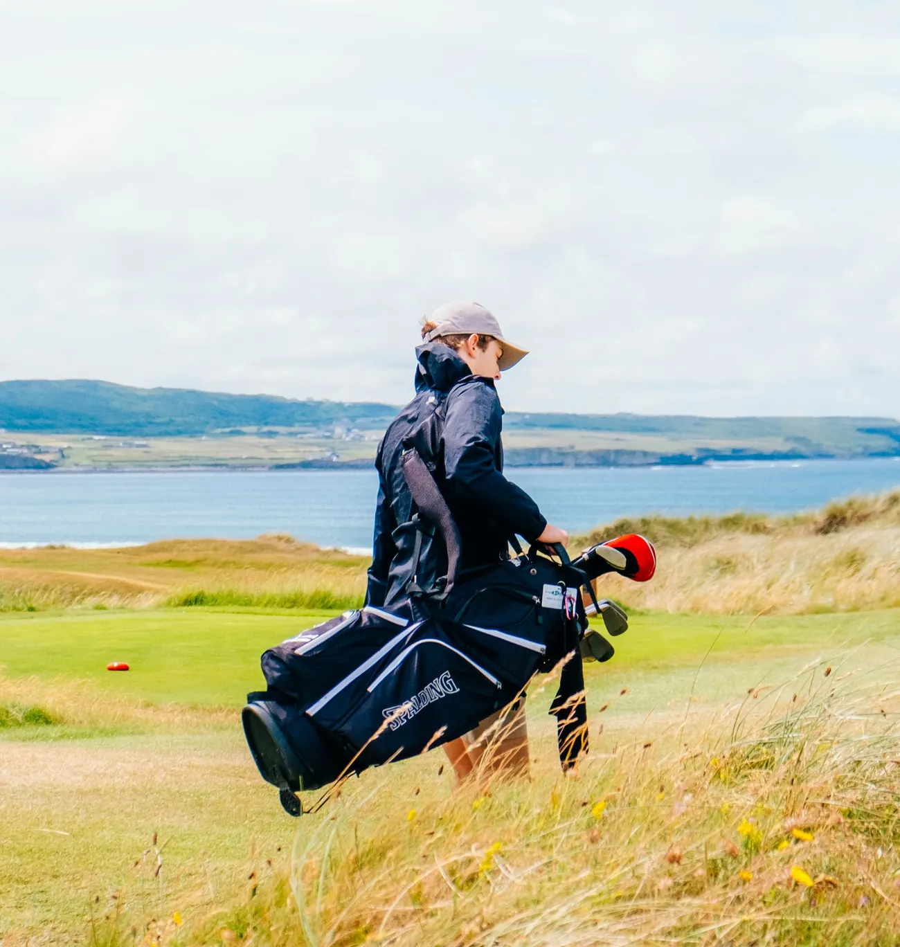 A golfer carrying a bag across a coastal links course
