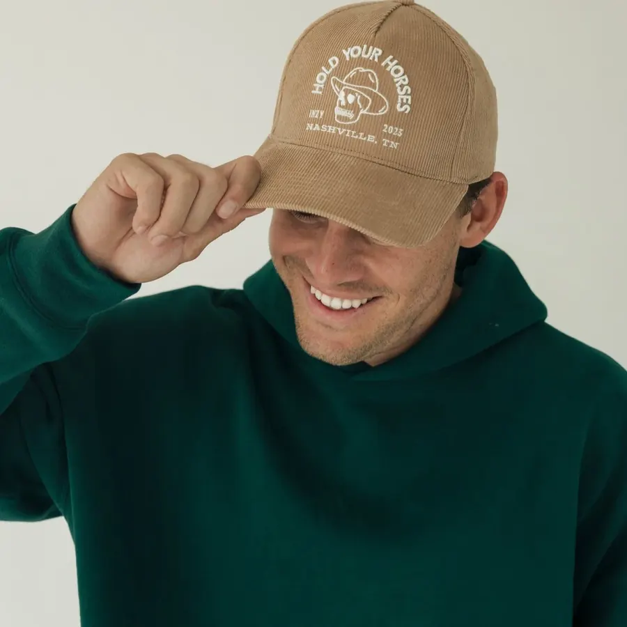 A man in a green hoodie adjusting an embroidered Inzy cap