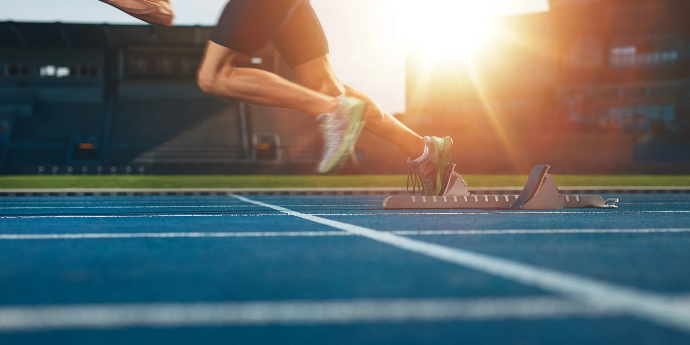 A sprinter pushing off the starting blocks on a track at sunrise
