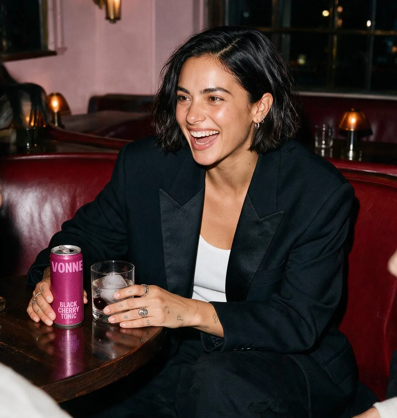 A woman laughing in a restaurant booth holding a canned drink