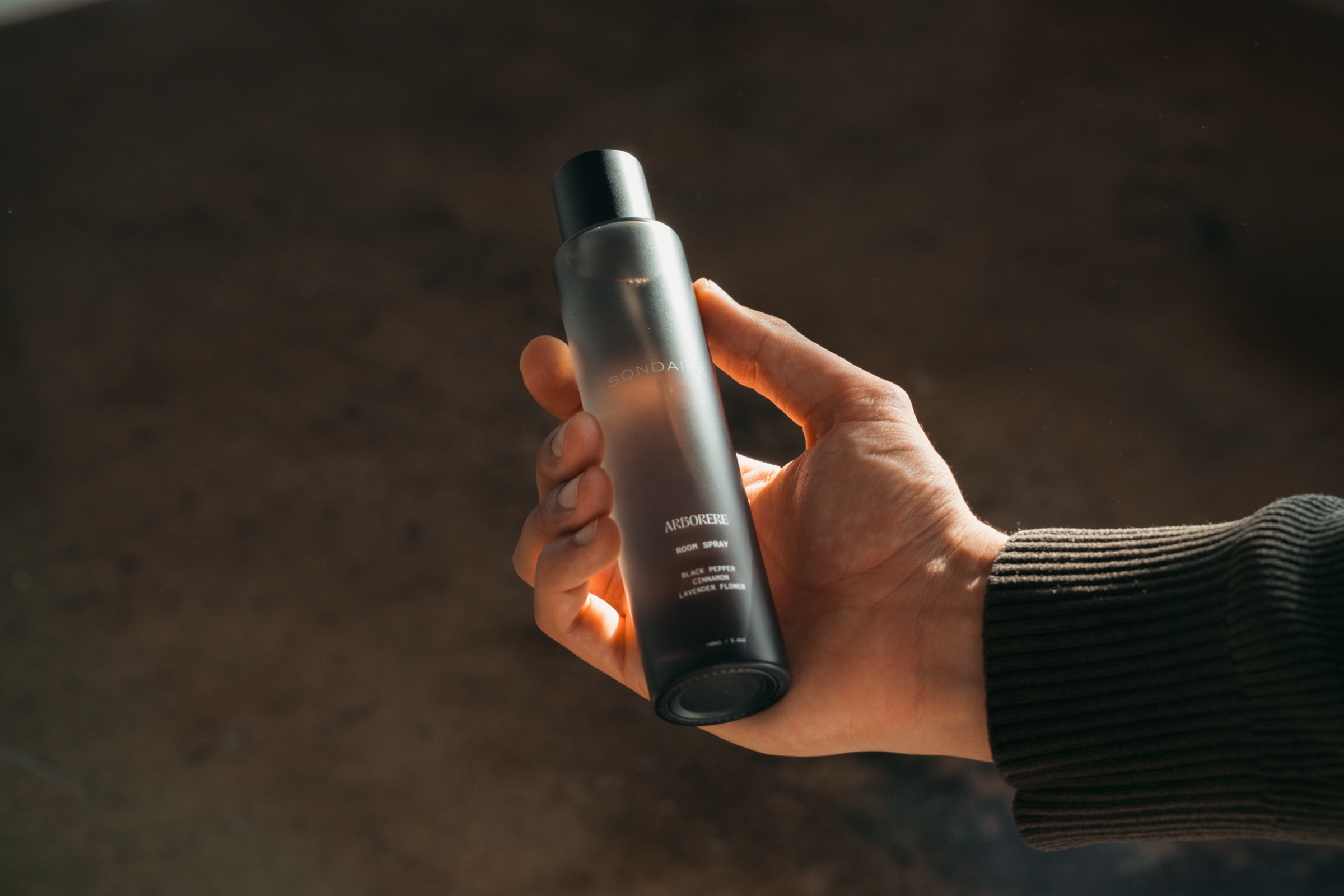 A hand holding a Sondaire Arborere room spray in low light