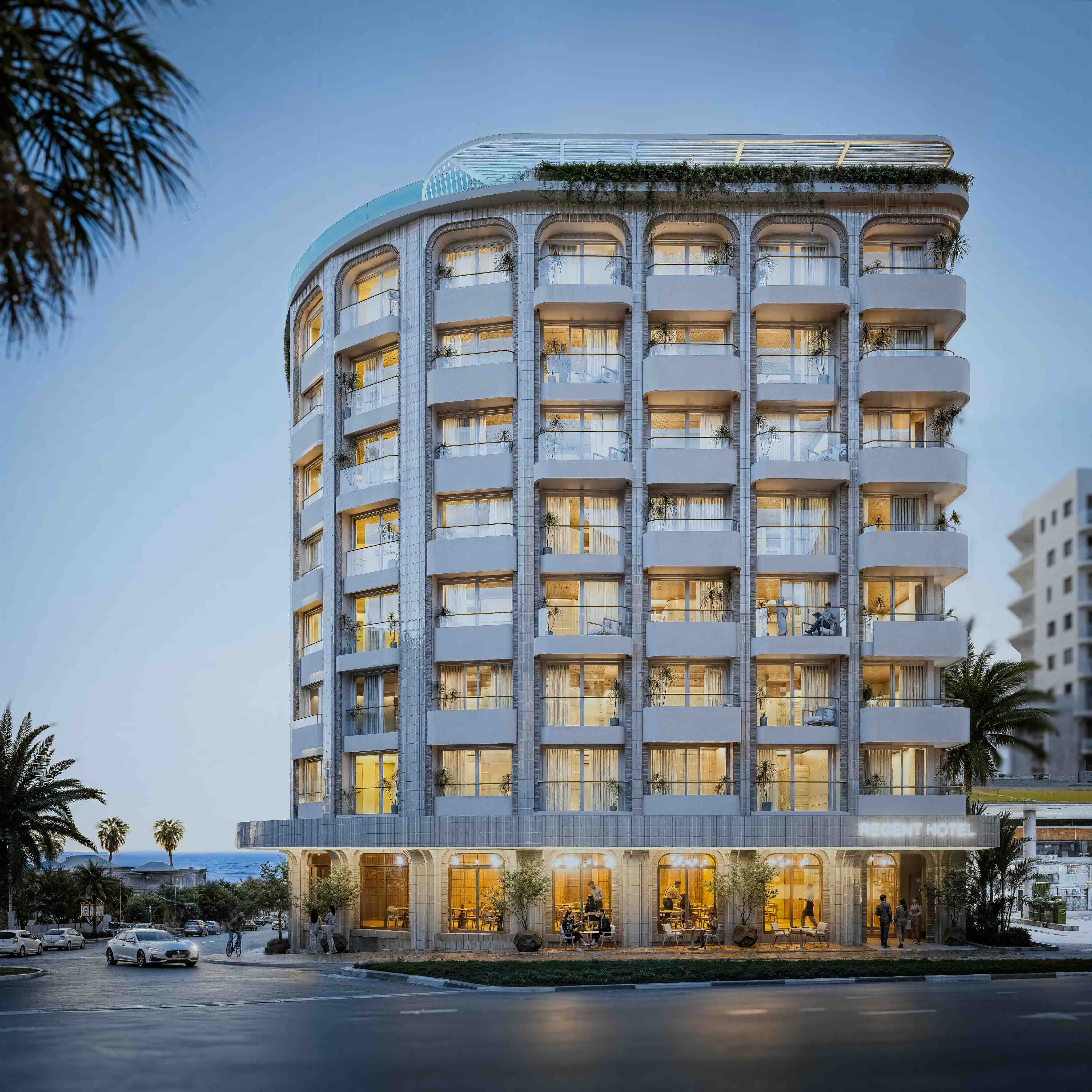 Modern multi-story hotel building with rounded edges and balconies on each floor, illuminated warmly in the evening, with palm trees and parked cars nearby, and the sign 'Regent Hotel' visible on the ground level.