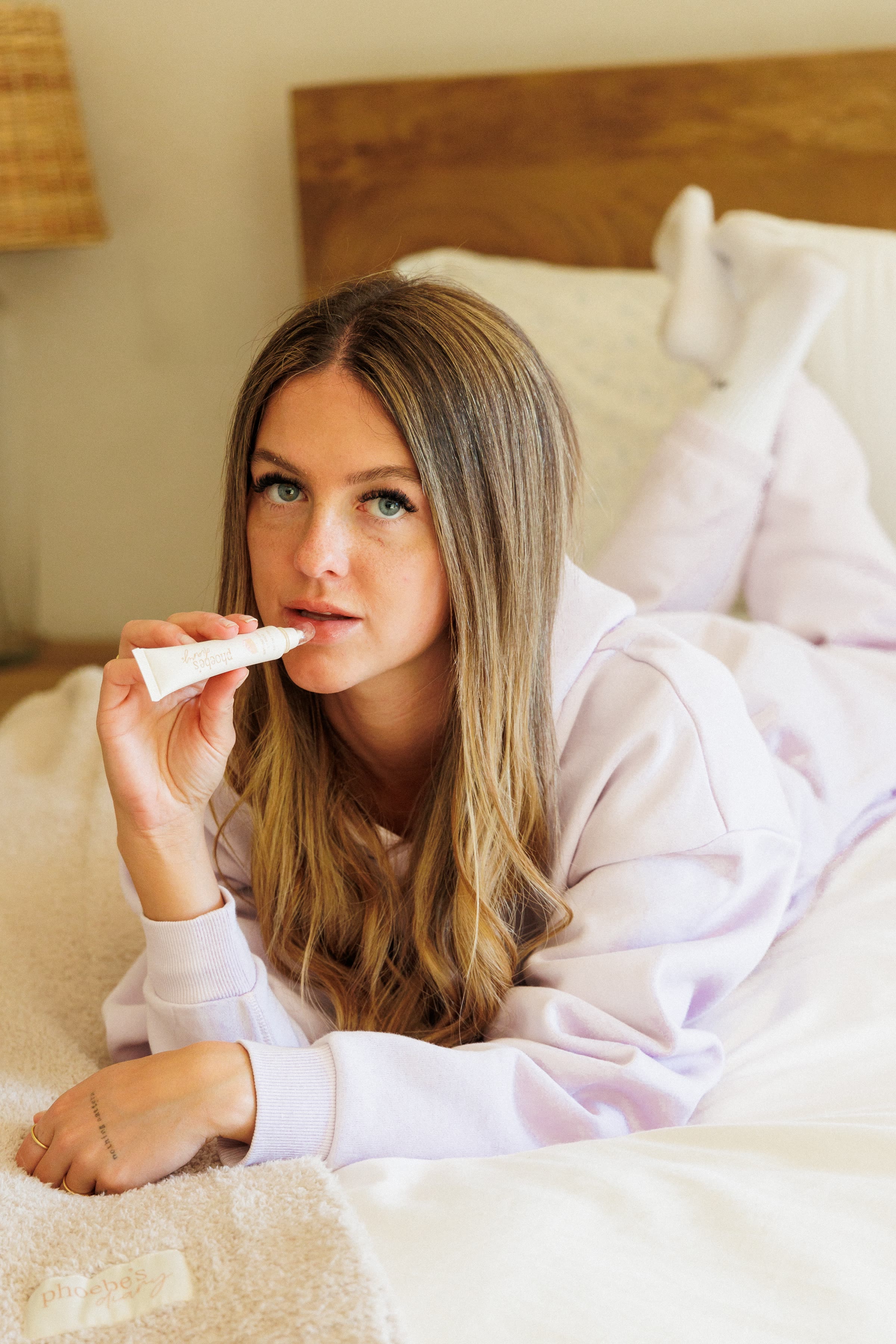 A creator in lilac loungewear applying Phoebe's Diary lip balm on a bed