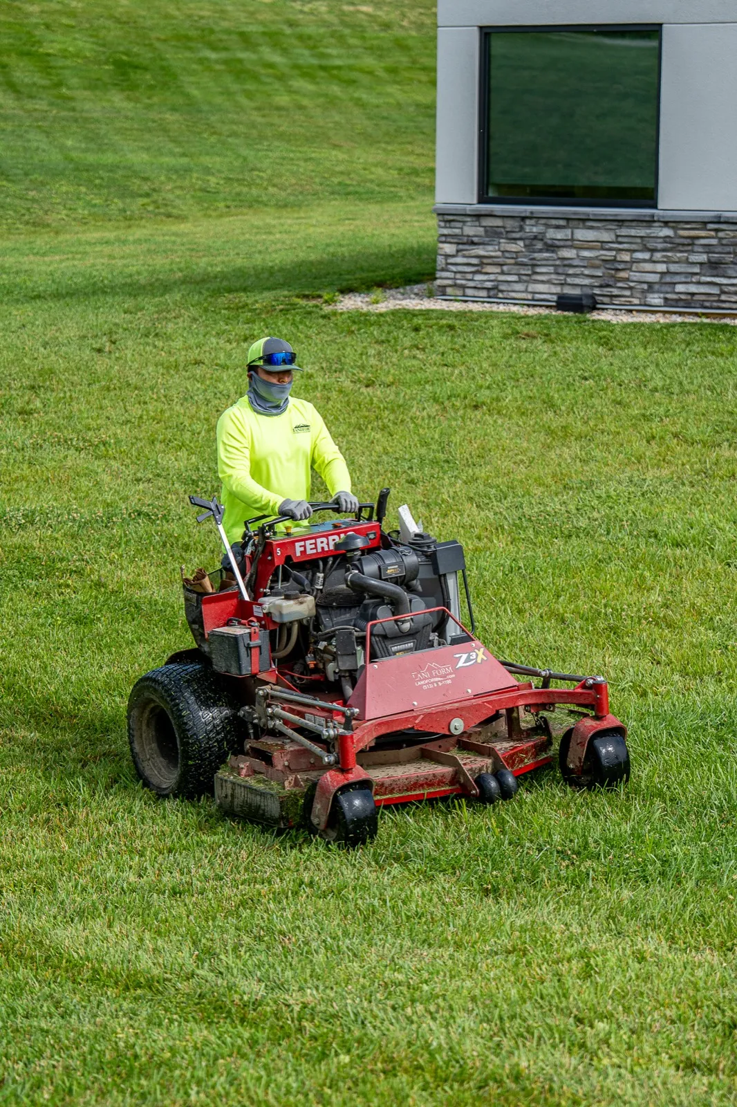 A Landform crew member cutting striped turf on a branded Ferris stand-on mower beside a commercial building