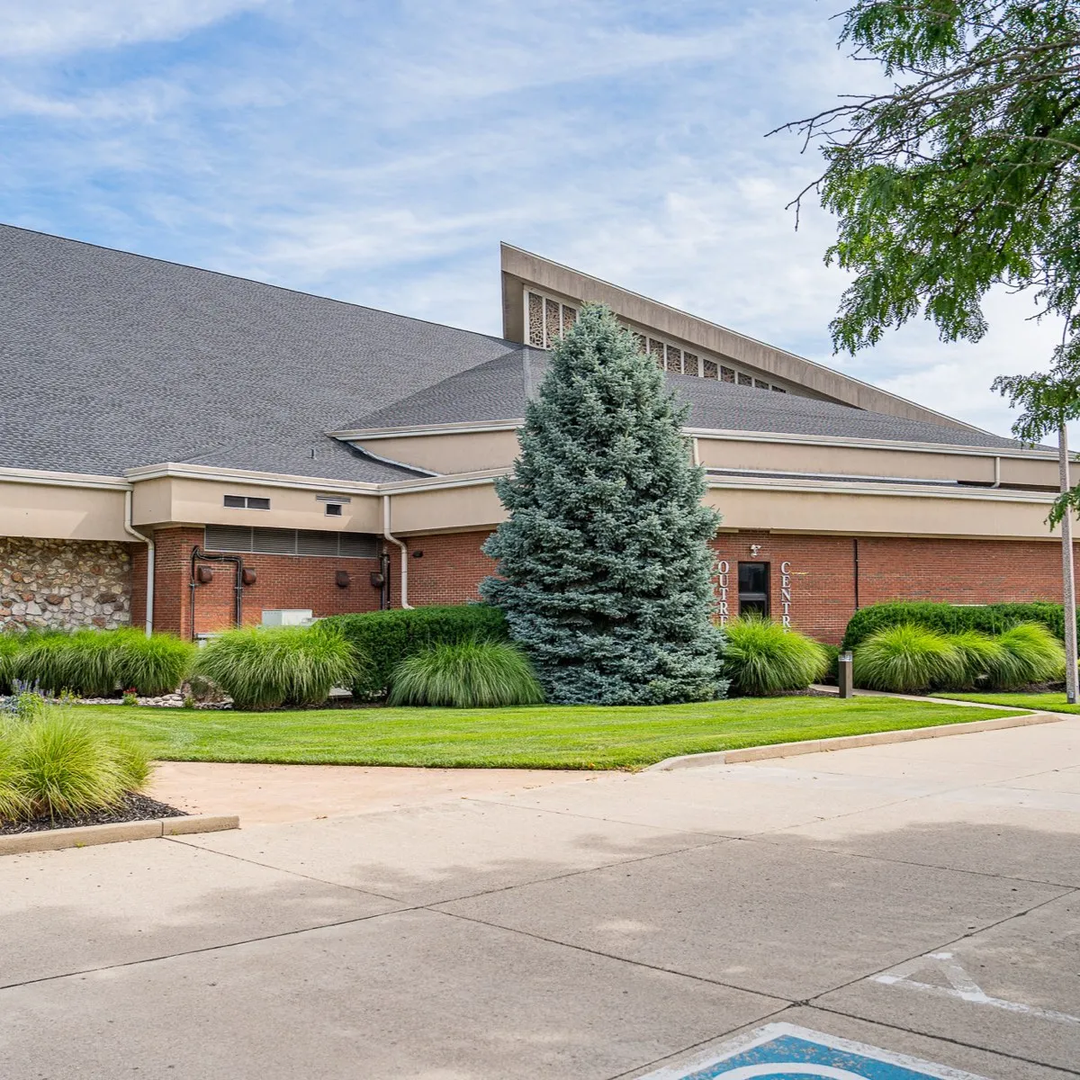 A church campus with trimmed foundation shrub beds, a blue spruce and a clean entrance drive