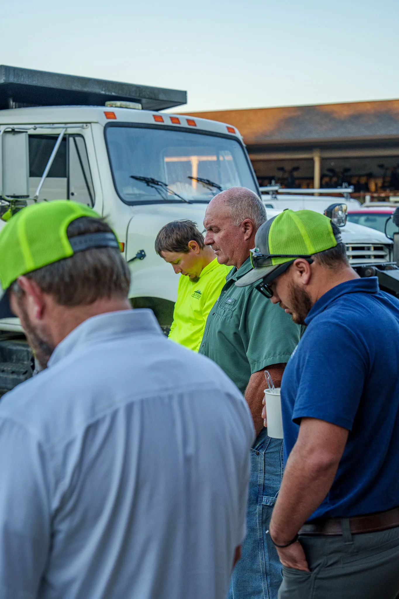 Landform team members gathered with heads bowed for the morning huddle beside the trucks at dawn