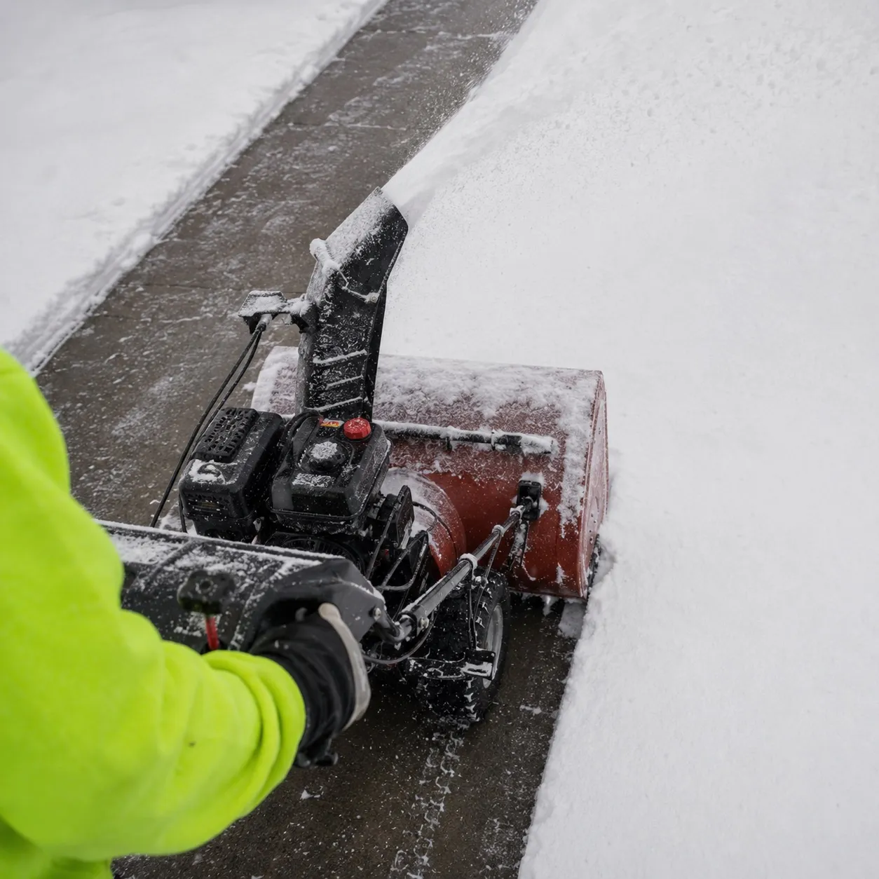 A crew member in hi-vis guiding a two-stage snow blower along a walkway, cleared pavement in its wake