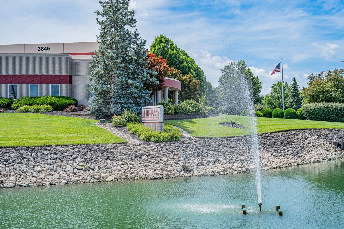 A commercial office building with maintained lawn, foundation plantings, and a fountain pond