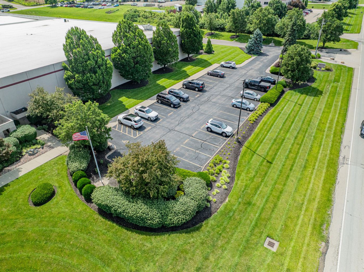 Aerial view of a commercial campus with freshly striped lawn, trimmed shrub beds, and a tree-lined parking lot
