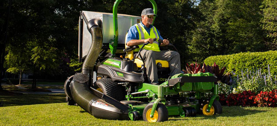 An operator in a safety vest mowing a commercial lawn on a zero-turn mower