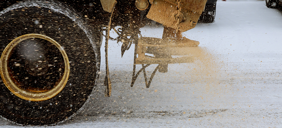A spreader truck throwing salt onto a snowy road