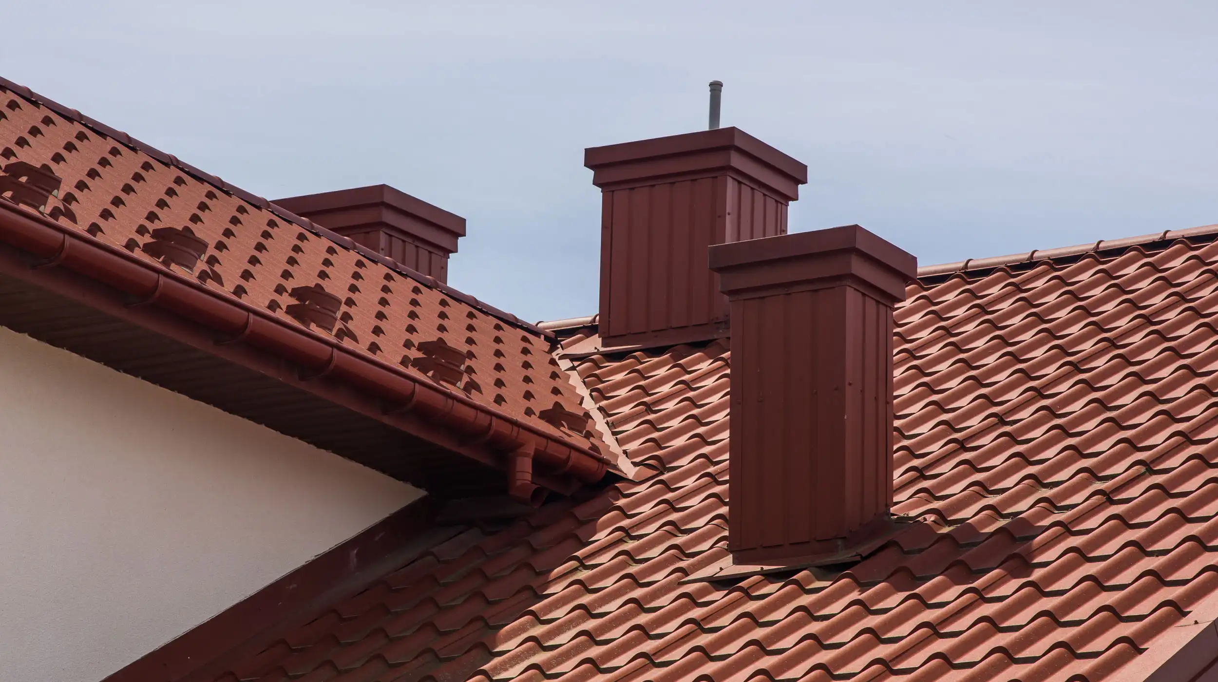 Red clay tiled roof with multiple chimneys and guttering on residential house