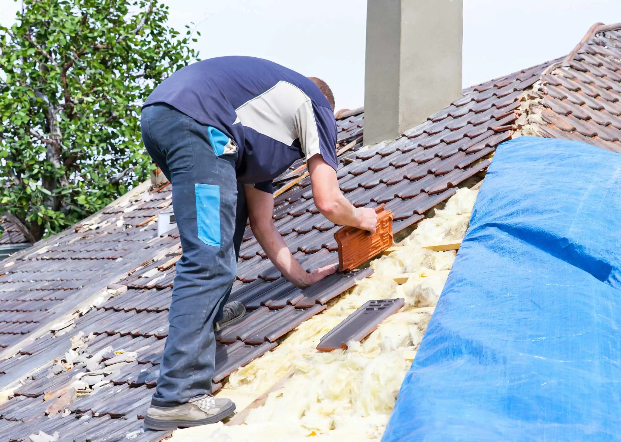 Technician replacing roof tiles and installing insulation on pitched residential roof during repair work
