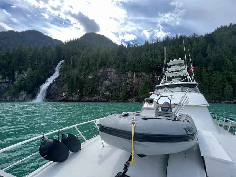 Surfrider's bow and tender in front of a waterfall and forested cliffs.