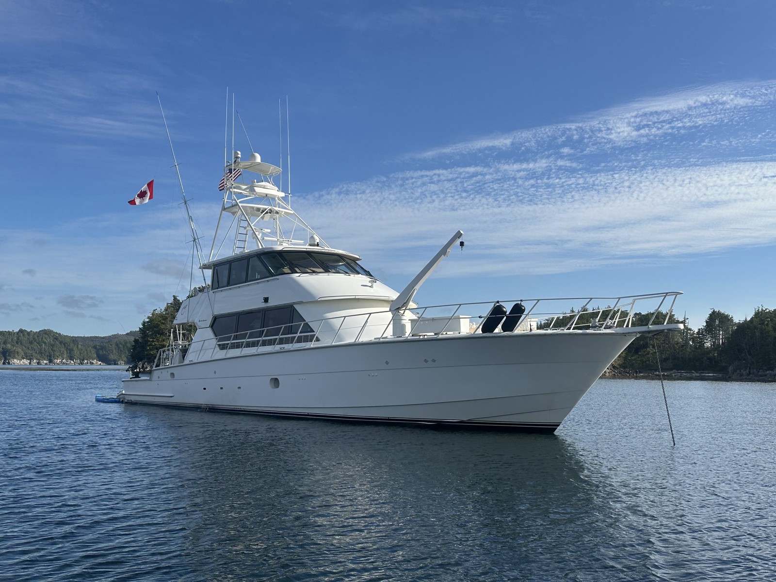 Surfrider at anchor on calm water beneath a blue sky, with wooded shoreline behind