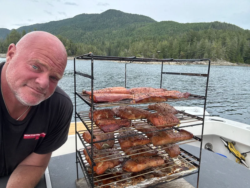 A person beside racks of fish cooking outdoors aboard the yacht.