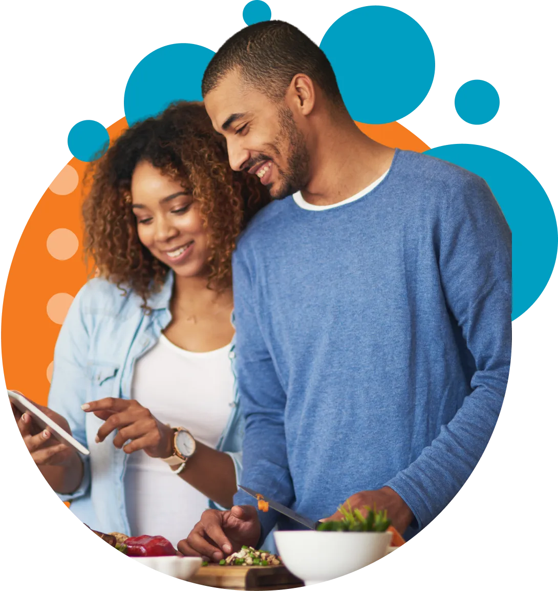 A man and woman smiling and preparing food together; the woman is holding a phone while the man chops vegetables on a cutting board.