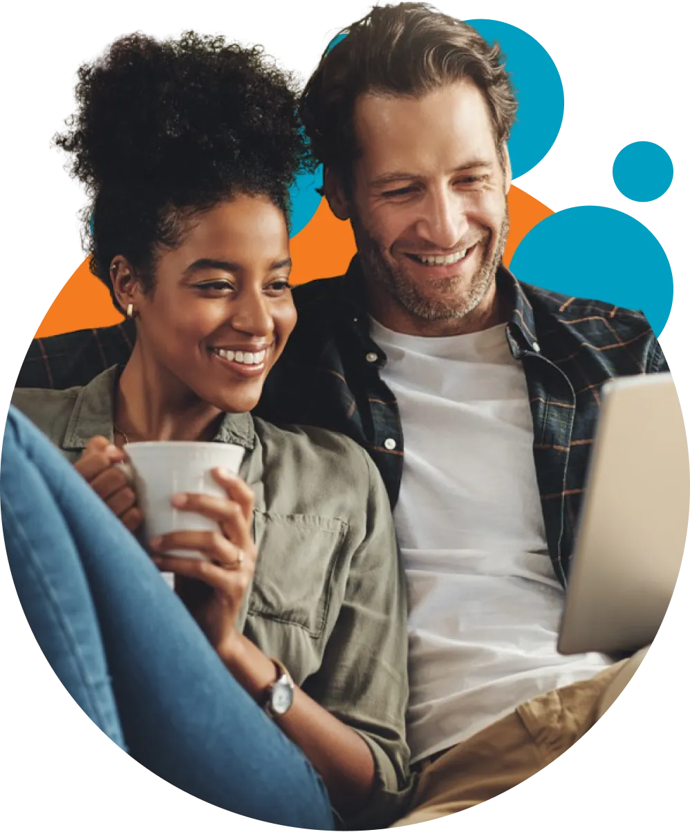 Smiling man and woman sitting close together, looking at a laptop screen, with the woman holding a white mug.