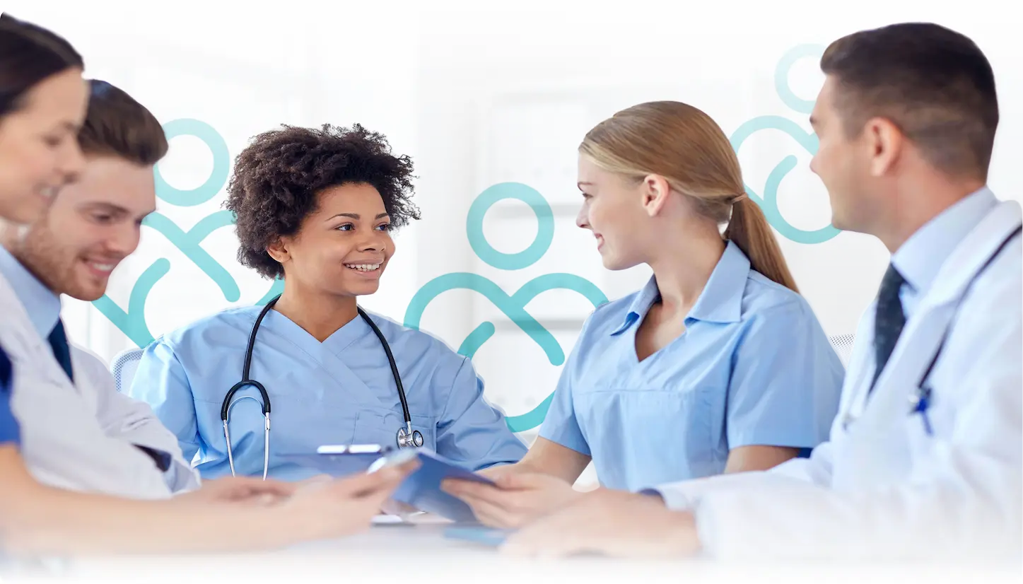 A diverse group of medical professionals including doctors and nurses, smiling and discussing information from a clipboard in a bright clinical setting.
