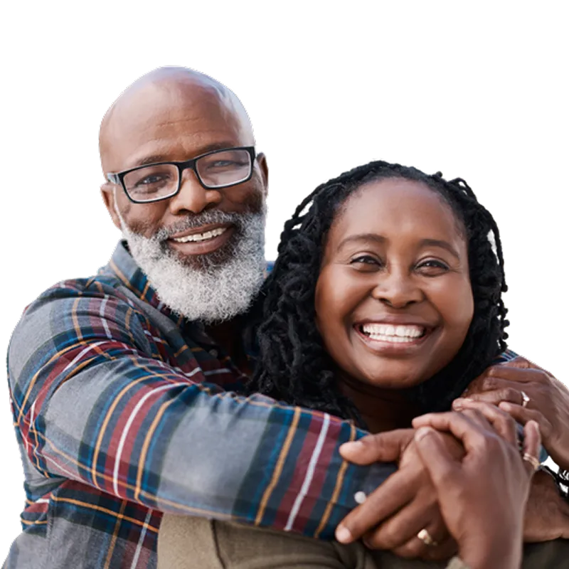 Smiling mature couple embracing each other, with the man wearing glasses and a plaid shirt and the woman with braided hair and a beige sweater.