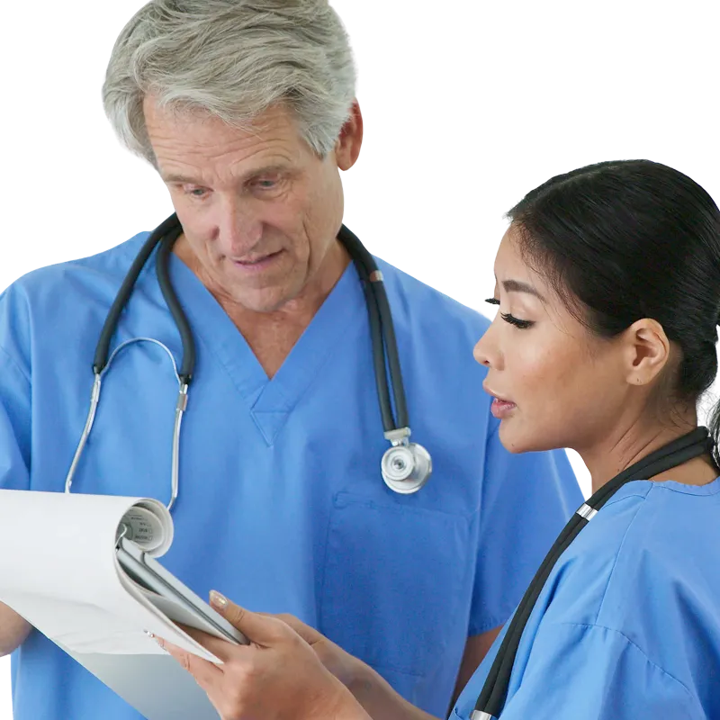 Two healthcare professionals wearing blue scrubs and stethoscopes discuss and review medical documents together.
