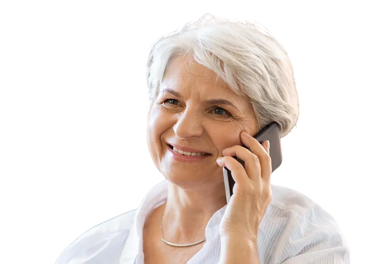 Smiling elderly woman with short white hair talking on a smartphone, wearing a white blouse and a curved silver necklace.