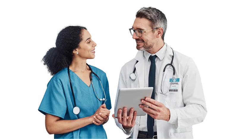 A male doctor in a white coat with a stethoscope holds a tablet and talks with a smiling female nurse in blue scrubs, also with a stethoscope.