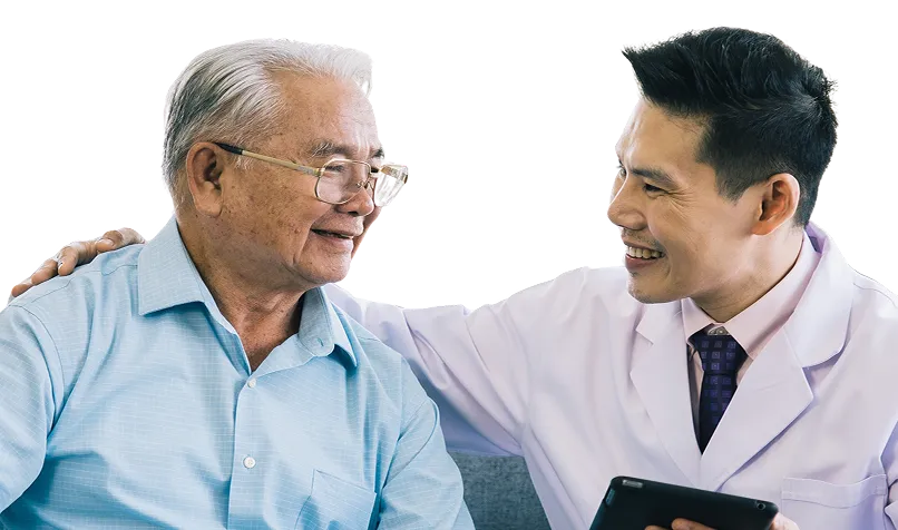 Smiling elderly man with gray hair and glasses in a blue shirt sitting next to a smiling male doctor in a white coat holding a tablet and placing a hand on the man's shoulder.