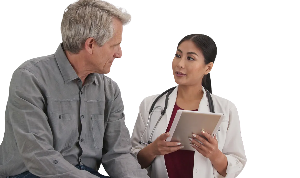 Female doctor with stethoscope around her neck holding a tablet and talking to an older male patient wearing a gray shirt.