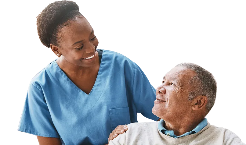 Smiling female healthcare worker in blue scrubs gently touching the shoulder of an older man in a beige sweater, both looking at each other warmly.