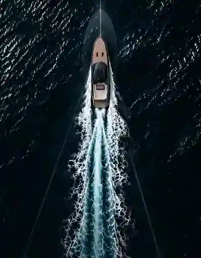 A motorboat moving swiftly through dark blue water, creating a V-shaped white wake behind it, captured from an overhead perspective.
