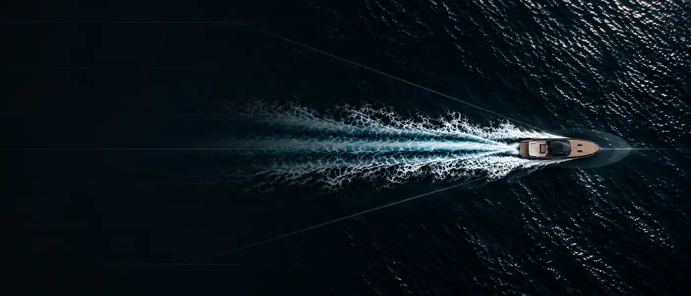 Aerial view of a boat speeding through dark water, leaving a white and turquoise foamy wake behind.