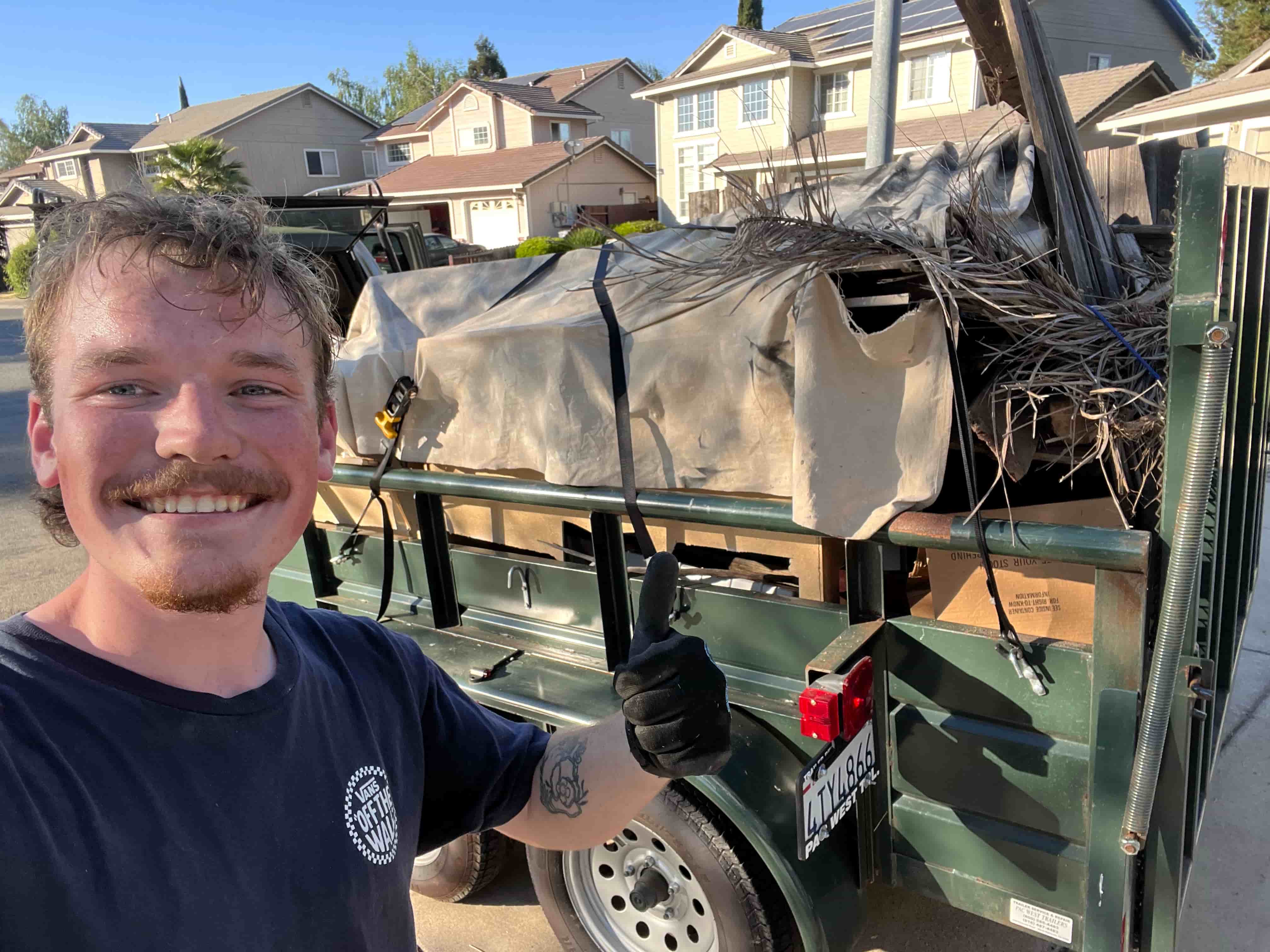 Aidan, owner of ATS Junk Removal, with a tarped and strapped trailer load of brush and household junk
