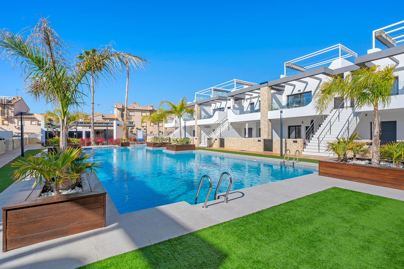 Gemeenschappelijk zwembad in lagunestijl met palmbomen en een gazon bij Innova Beach, Orihuela Costa, de locatie van Casa 50 Marina