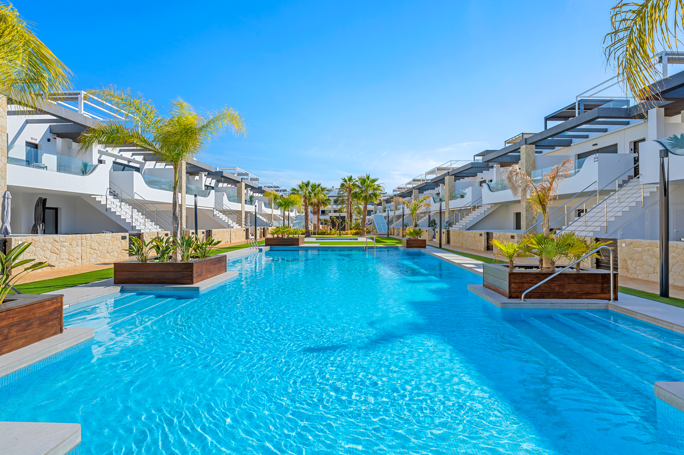 Groot gemeenschappelijk zwembad met palmbomen bij Innova Beach, Orihuela Costa, de locatie van Casa 48 Azul