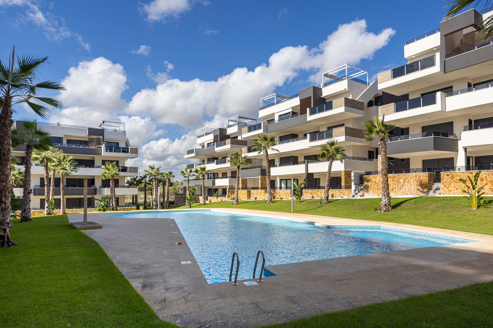 Lang gemeenschappelijk zwembad met gazon en palmbomen bij Amanecer XI, Orihuela Costa, de thuisbasis van Casa Vida Moderna