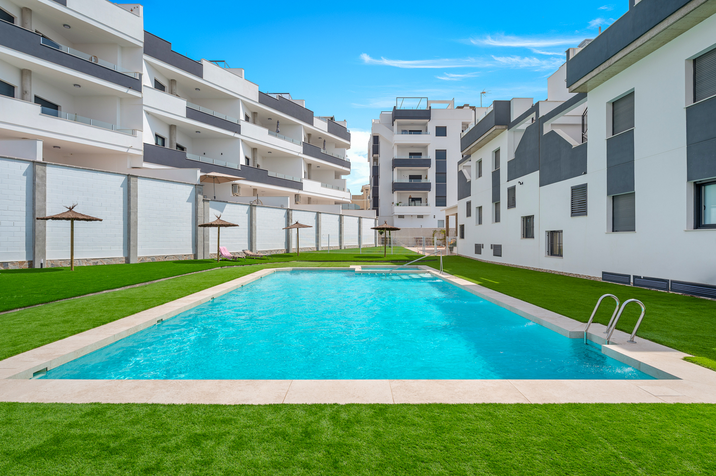 Gemeenschappelijk zwembad omringd door gazon en witte appartementen bij Sunset Hill, Orihuela Costa, de thuisbasis van Casa Solana