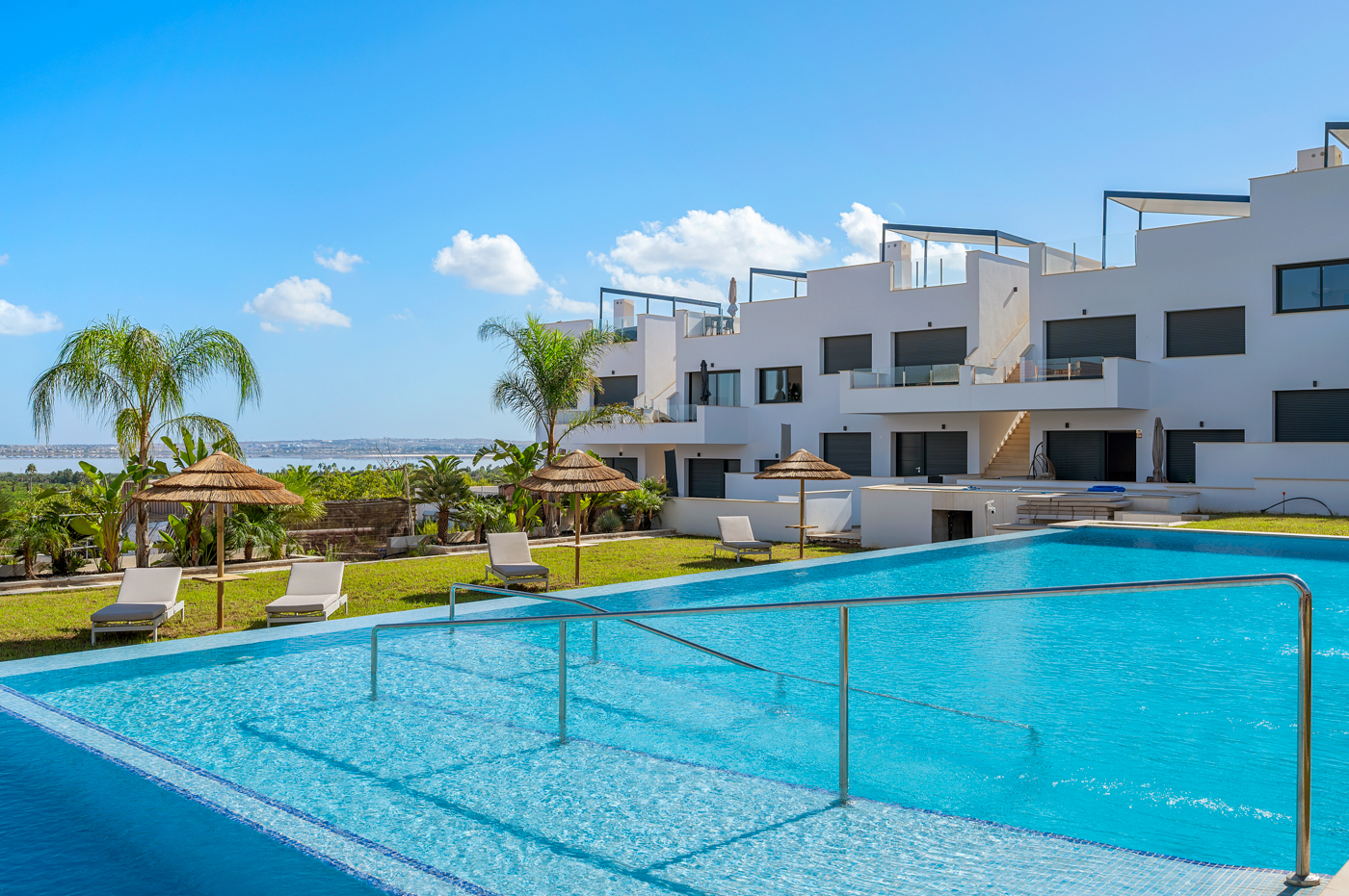 Gemeenschappelijk zwembad met palmbomen en ligbedden bij Residencial Onaru, Torrevieja, de locatie van Casa El Refugio