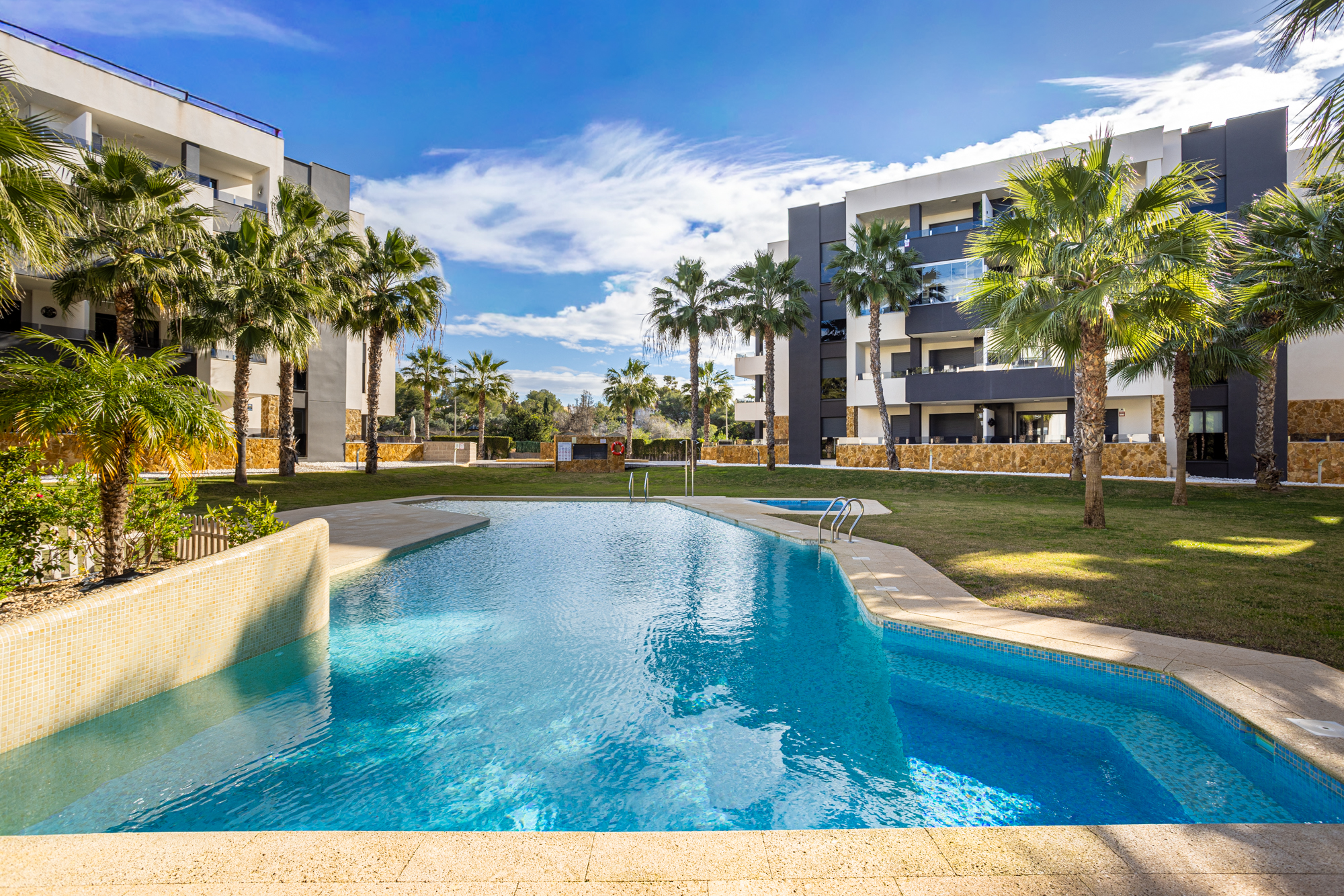 Gemeenschappelijk zwembad omzoomd door palmbomen bij Amanecer VI, Orihuela Costa, de thuisbasis van Casa Johna