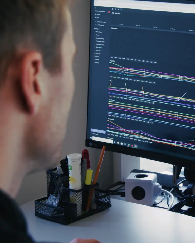 Man closely viewing a computer monitor displaying multiple colorful line graphs and data points on a dark interface.