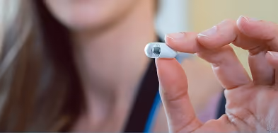 Close-up of a hand holding a small pill camera capsule used for pill cam endoscopy