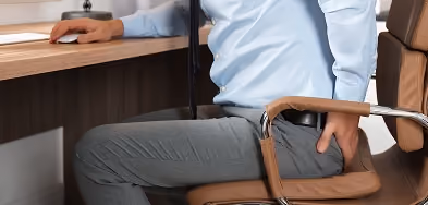 Man sitting in an office chair holding his lower back and hip in discomfort