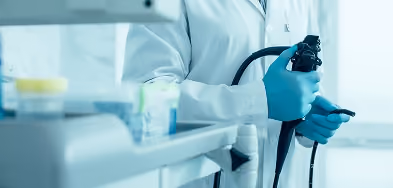 Close-up of a gloved hand holding an endoscope device used for a colonoscopy procedure