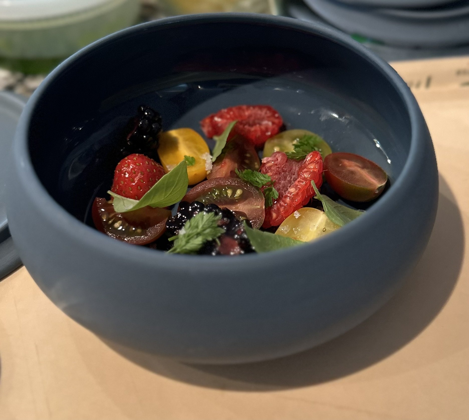 Heirloom tomatoes, berries and basil in a dark bowl