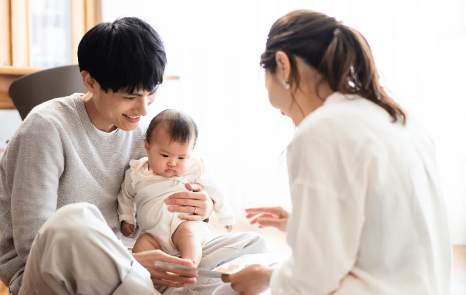 赤ちゃんを抱く父親とそばで見守る母親