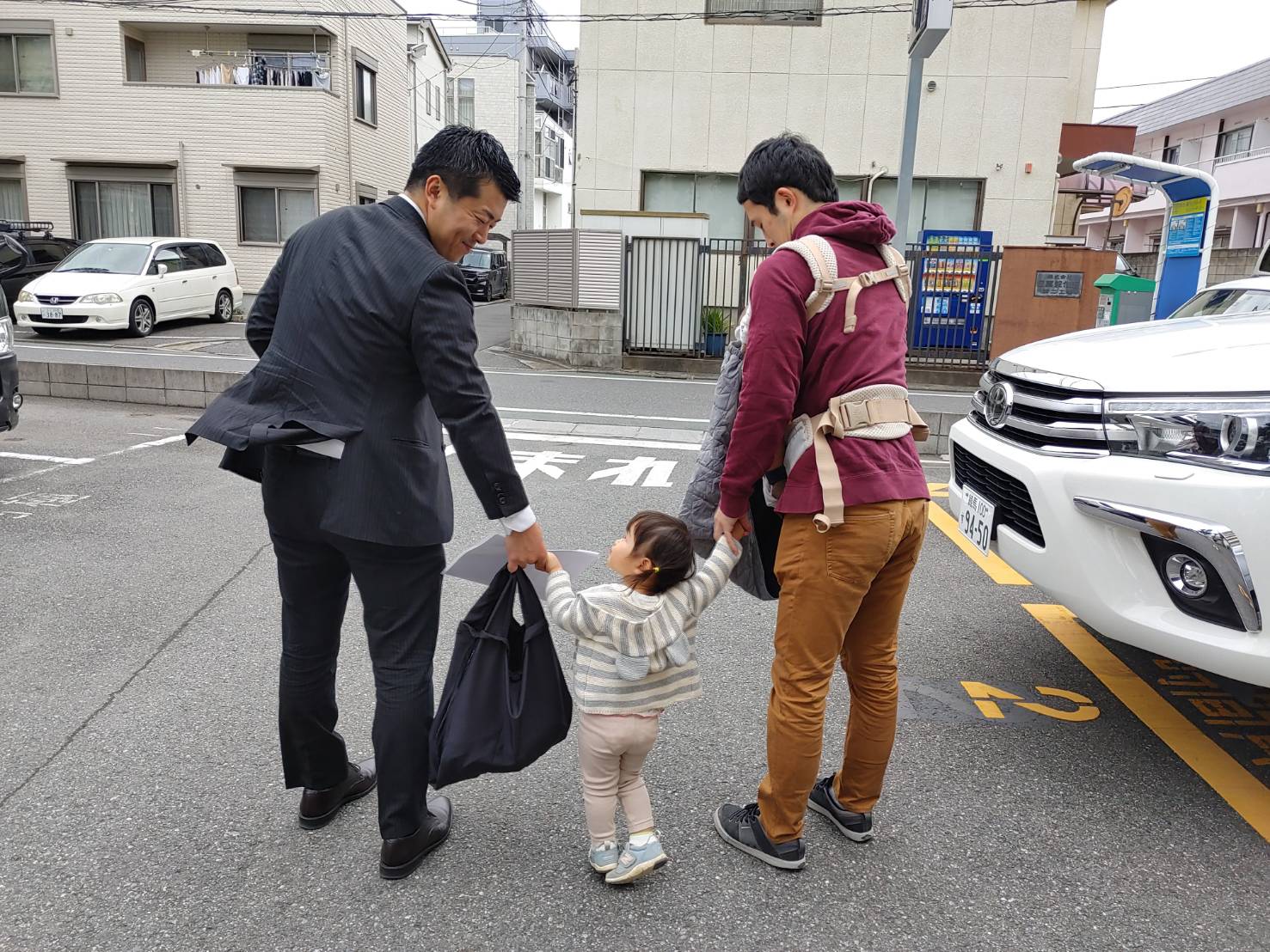 子どもと手をつないで歩く二人の大人