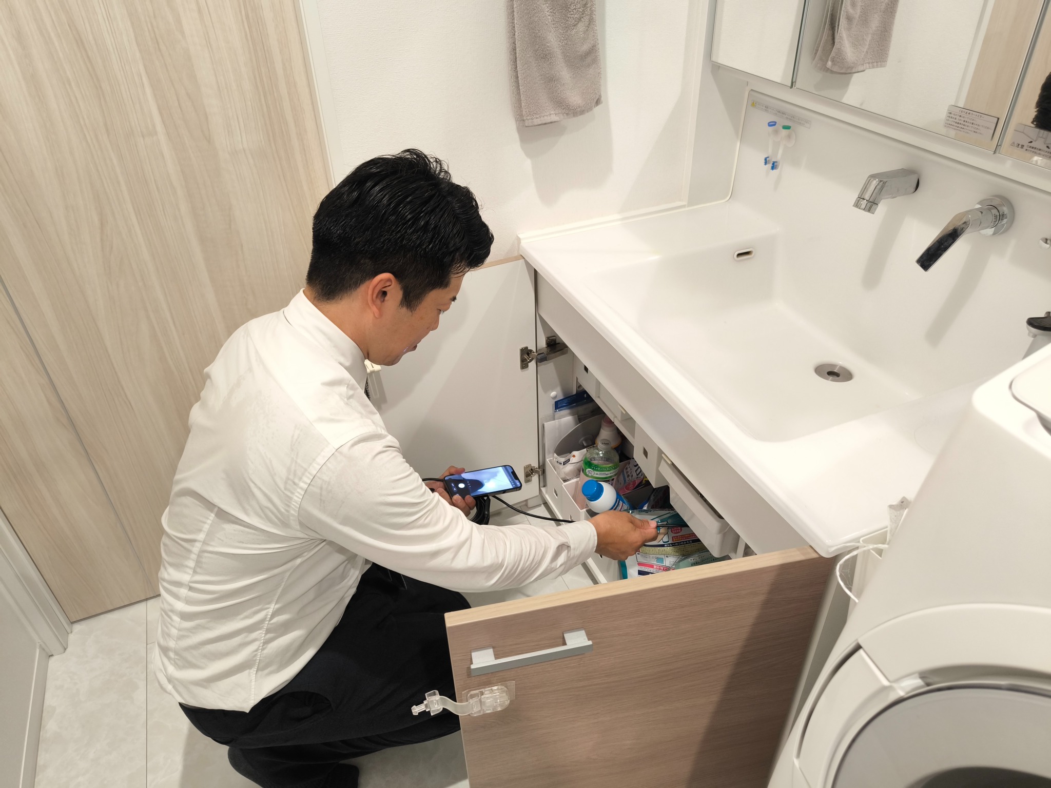 ファイバースコープとスマートフォンを使い洗面台下を確認するAIME担当者